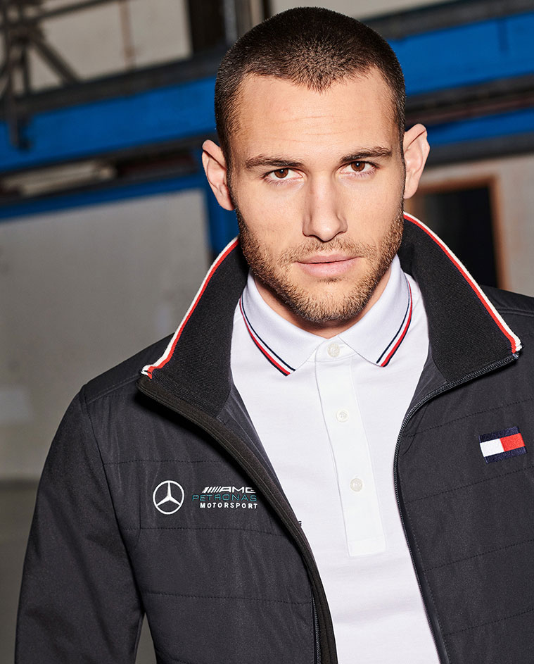 Male model wears sweatshirt and jacket, holds satchel bag, all from TOMMYXMERCEDES-BENZ collection.