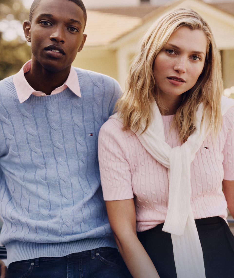 A male and female model wear lightweight cotton sweaters in pastel colors, new for spring from Tommy Hilfiger.