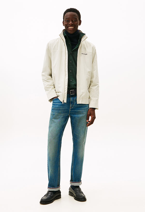 Model wearing a Tommy Hilfiger off-white sherpa jacket layered over a green hoodie, styled with light blue jeans and black shoes, standing against a white background.