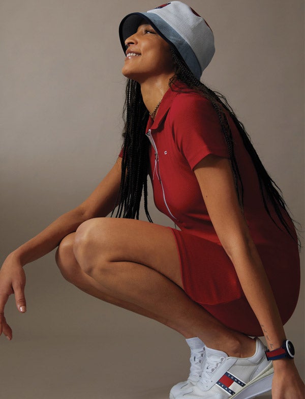 A female model wears a bucket hat paired with a red knit dress, new from Tommy Jeans.