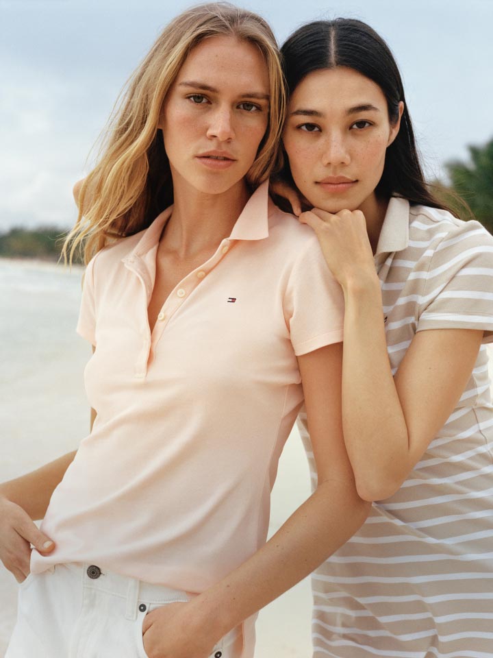 Two female models stand on the beach wearing the Tommy Hilfiger Stretch Cotton Polo and a polo dress.