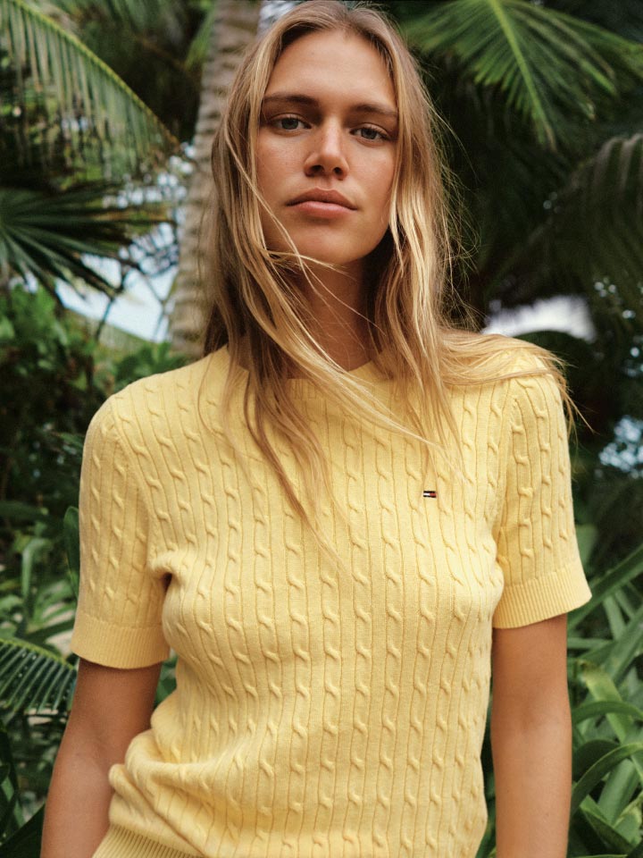 A female model wears the Tommy Hilfiger Cable Knit Short Sleeve Sweater in yellow.