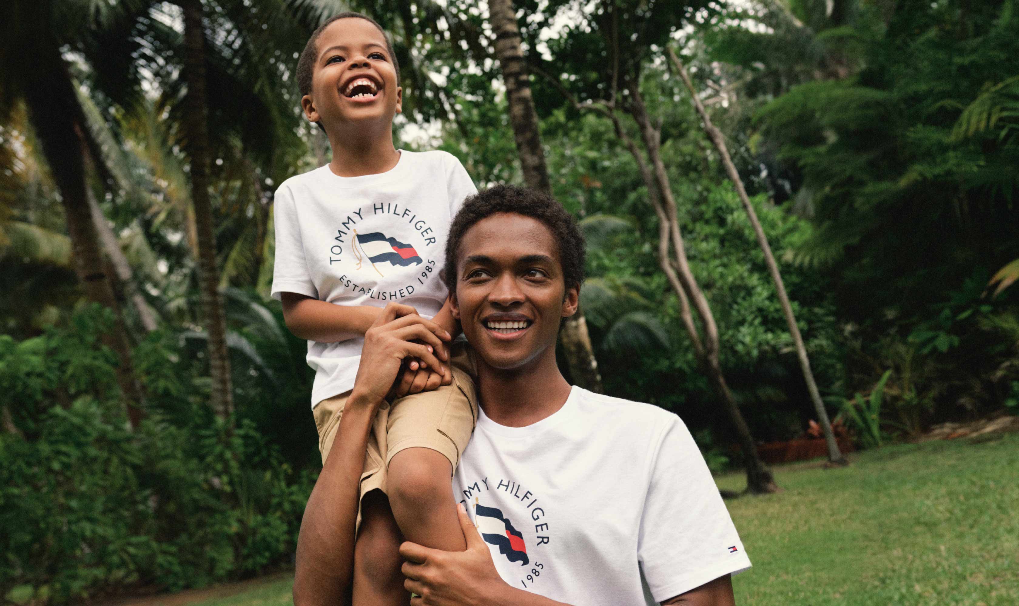 A father and son wear matching t-shirts from Tommy Hilfiger.