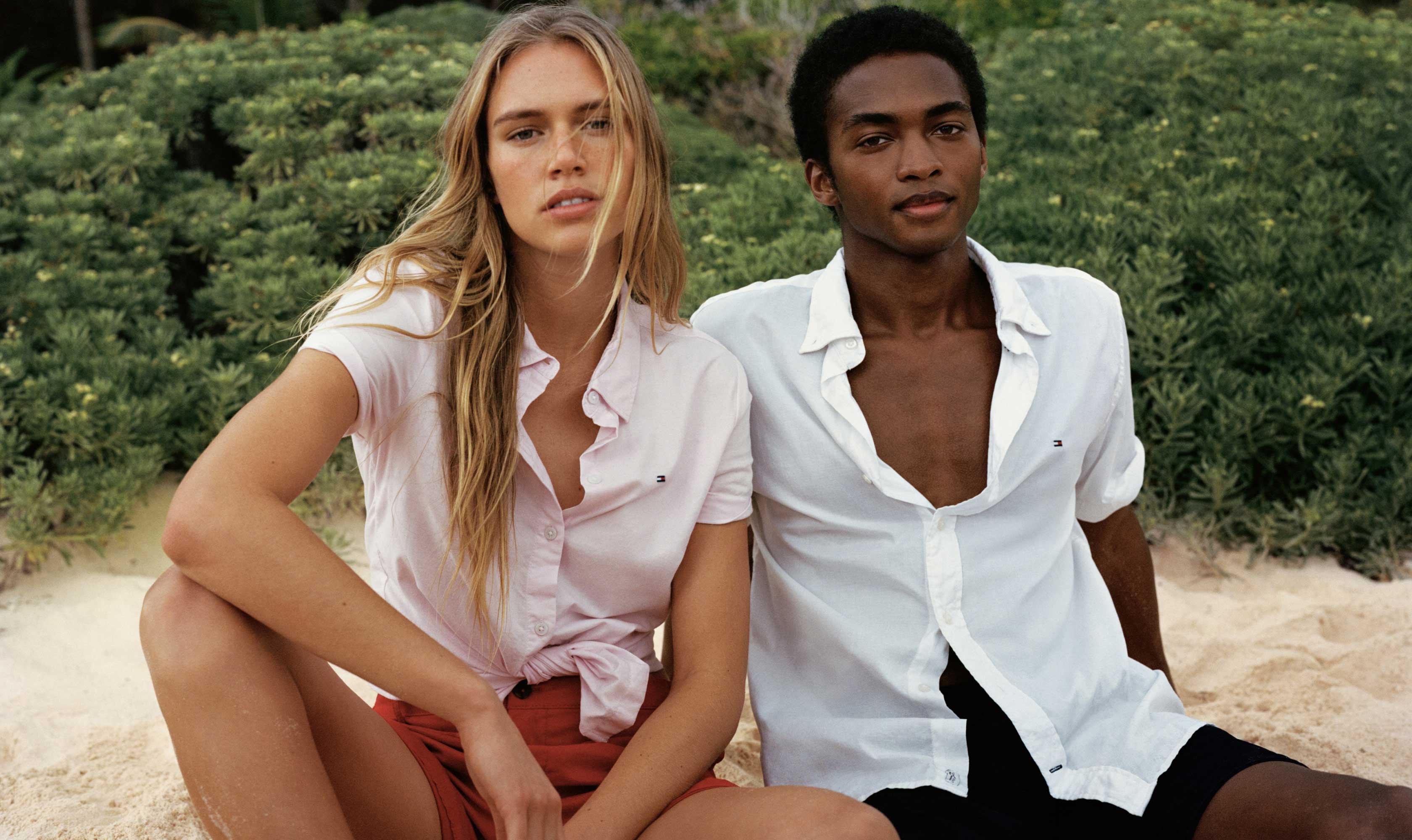 A male and female model wear Tommy Hilfiger linen shirts on the beach.
