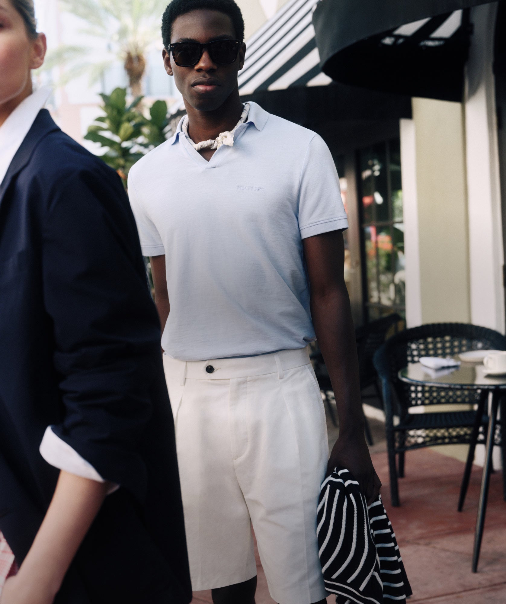 Man wearing Tommy Hilfiger polo and pants standing outside café