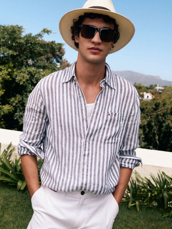 Man wearing sunglasses dressed in Tommy Hilfiger linen essentials standing with his hands in his pockets