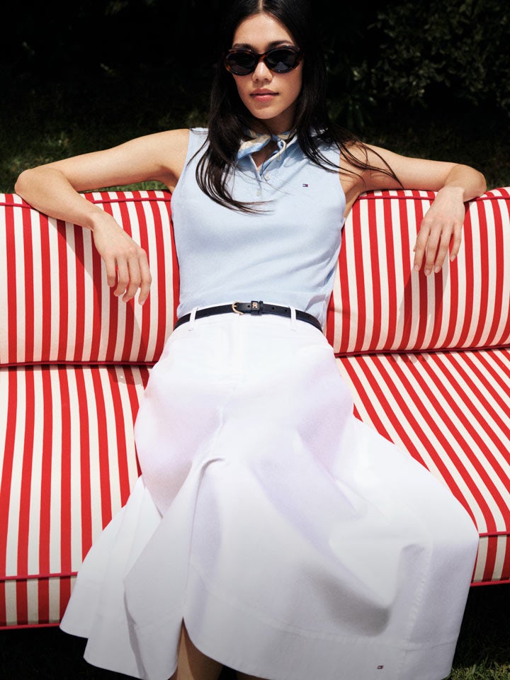 Woman sitting on striped couch wearing Tommy Hilfiger polo and skirt
