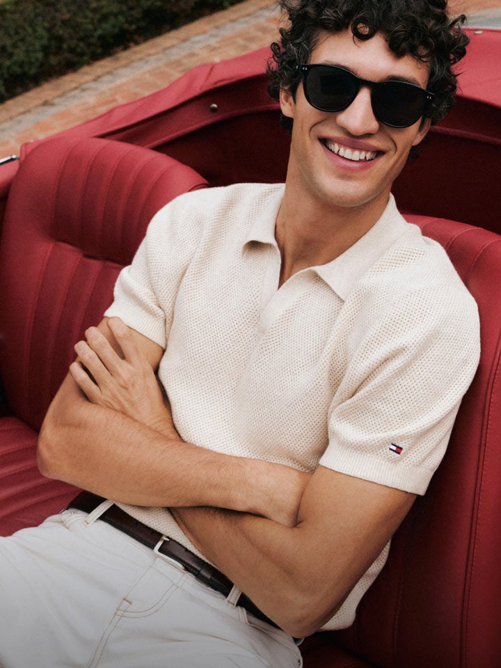 Man sitting in a car with his arms crossed wering Tommy Hilfiger polo shirt and pants