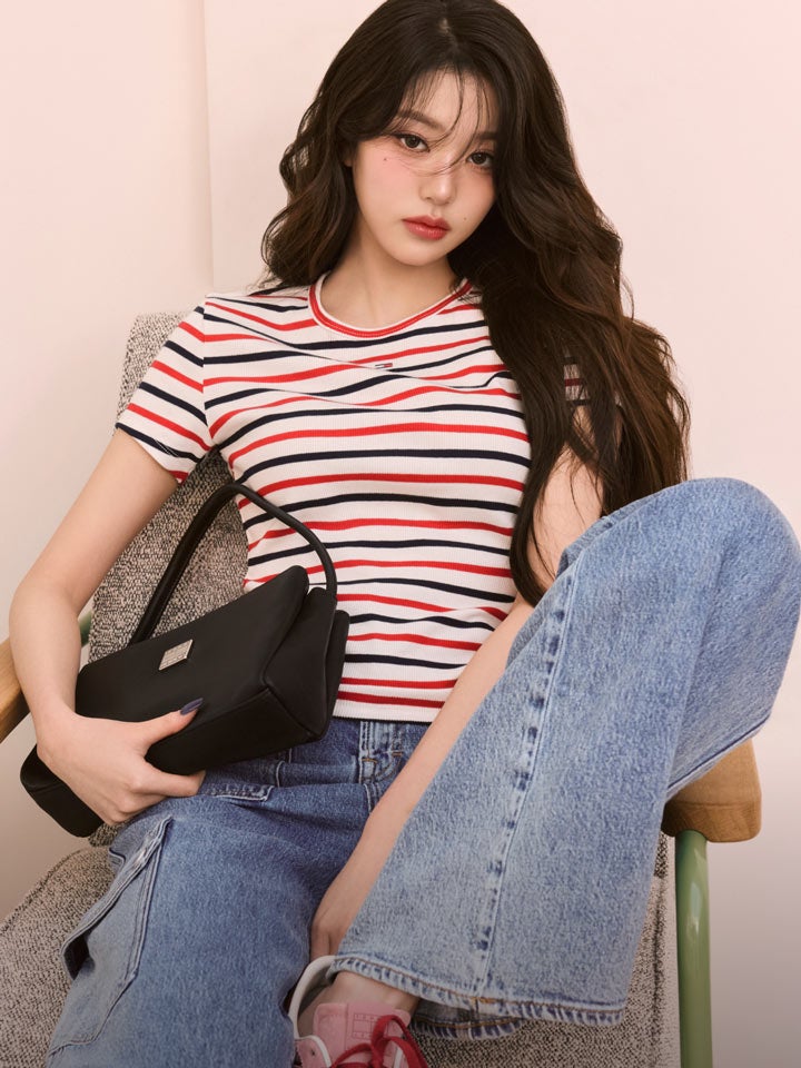 Won Young assis sur une chaise avec une jambe relevée vêtue d’une chemise Tommy Girl et d’un jean de Tommy Hilfiger
