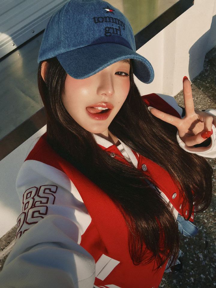 Woman taking selfie with fingers up wearing Tommy Girl hat and jacket by Tommy Hilfiger