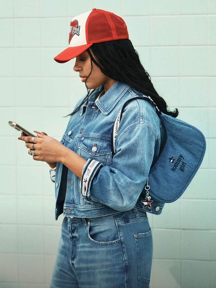 Woman side profile texting wearing Tommy Girl by Tommy Hilfiger hat, jacket and jeans