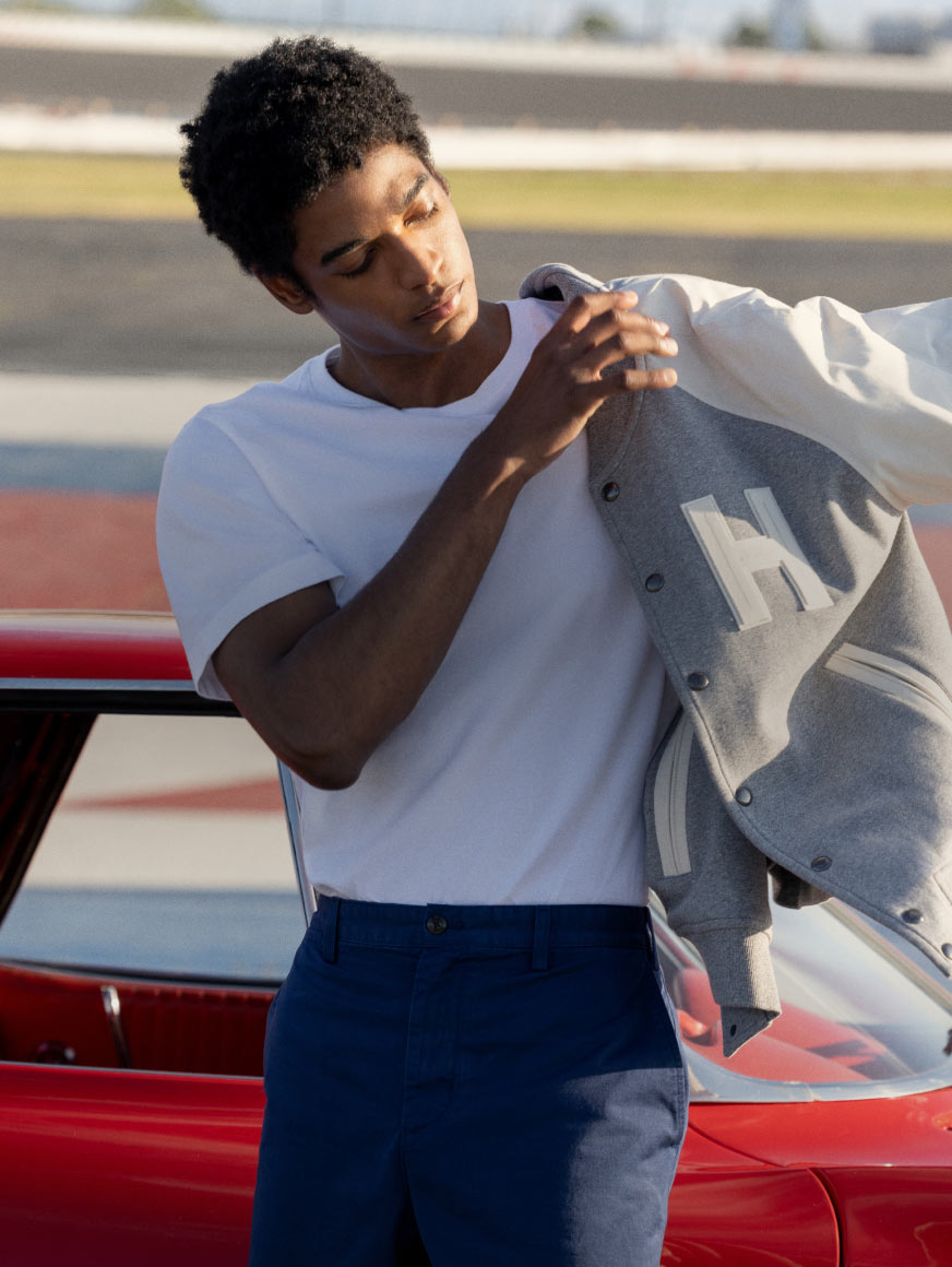 Man on racetrack putting on Tommy Hilfiger racing jacket while leaning on a car