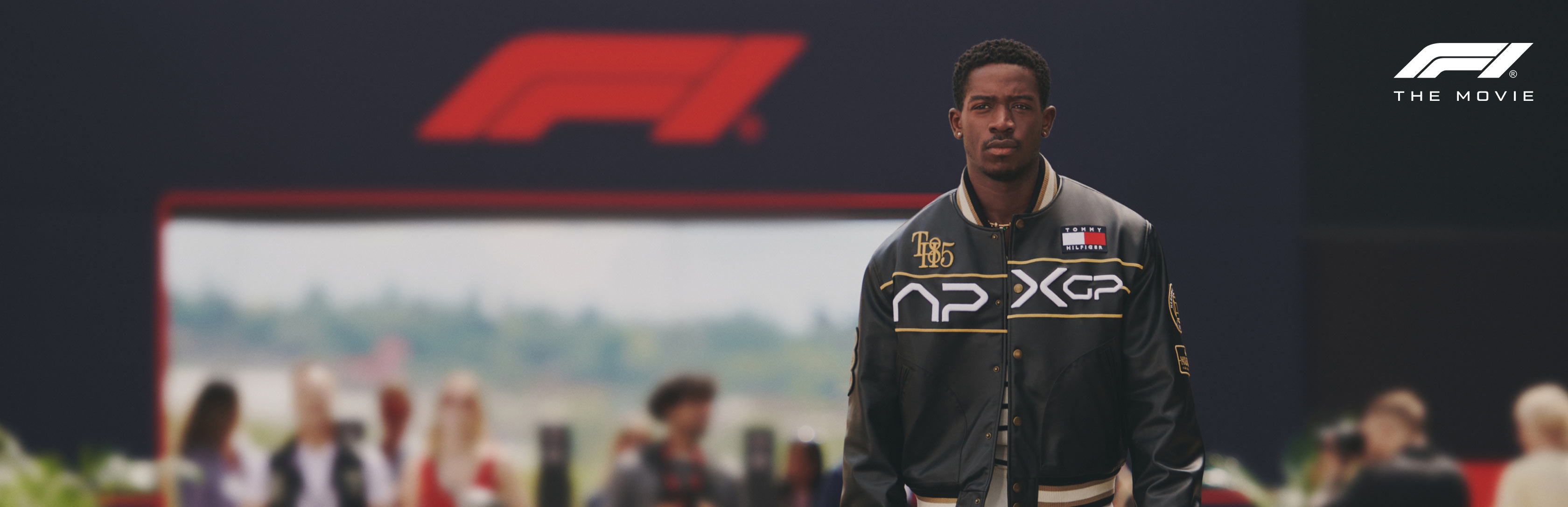 Damson Idris walking down the track in APXGP jacket with F1 logo behind him