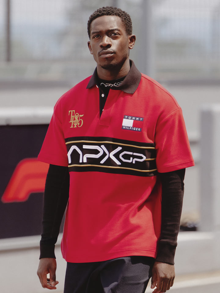 Damson Idris portant un polo surdimensionné APXGP rouge marchant sur la piste