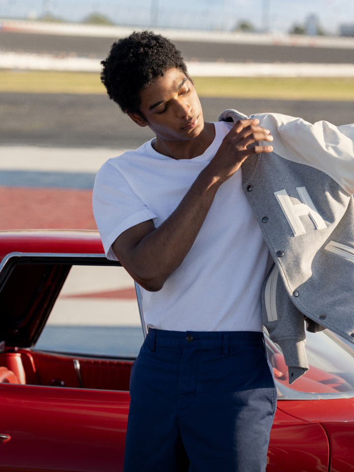 Man on racetrack putting on Tommy Hilfiger racing jacket while leaning on a car