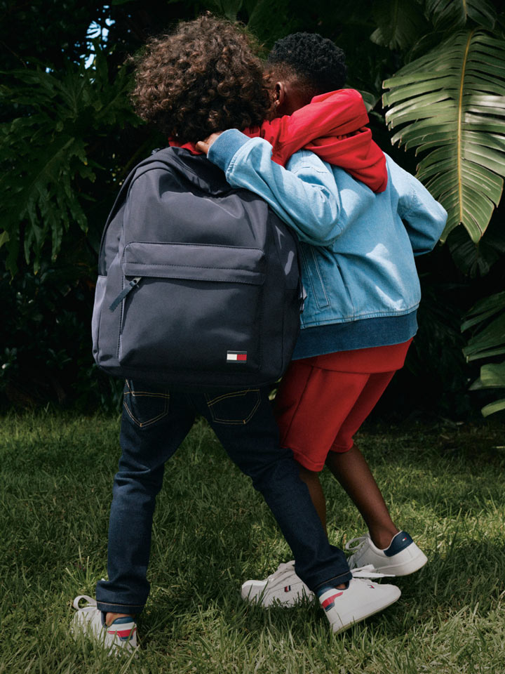 Two kids turned around with their arms around each other dressed in Tommy Hilfiger