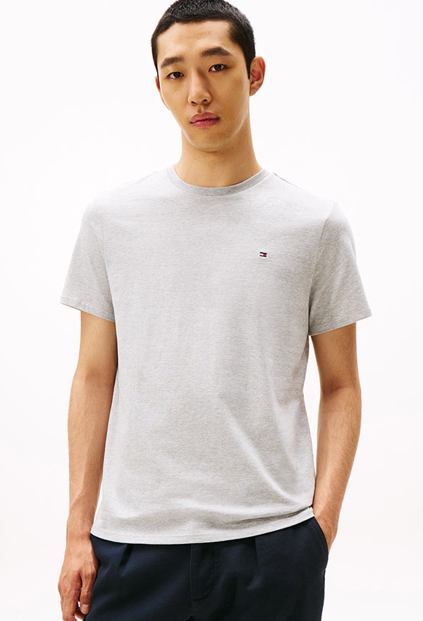 Model wearing a Tommy Hilfiger olive green short-sleeve polo shirt with contrast tipping, styled with white pants, against a white background