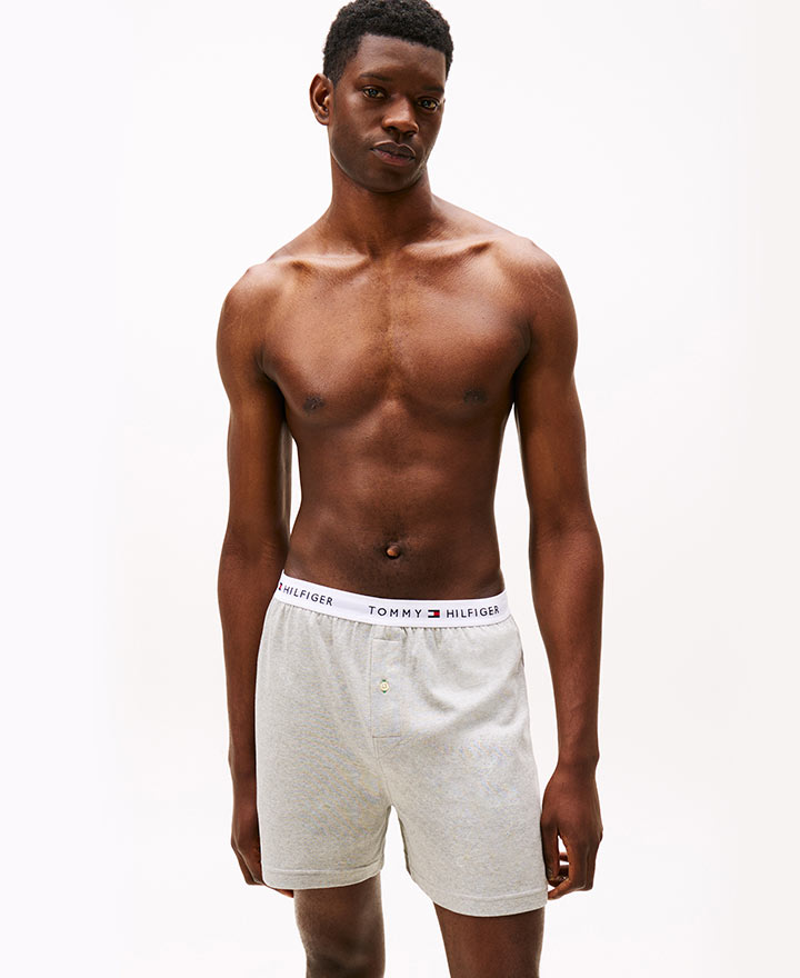 Model wearing Tommy Hilfiger white boxers with logo waistband, posed against a white background.
