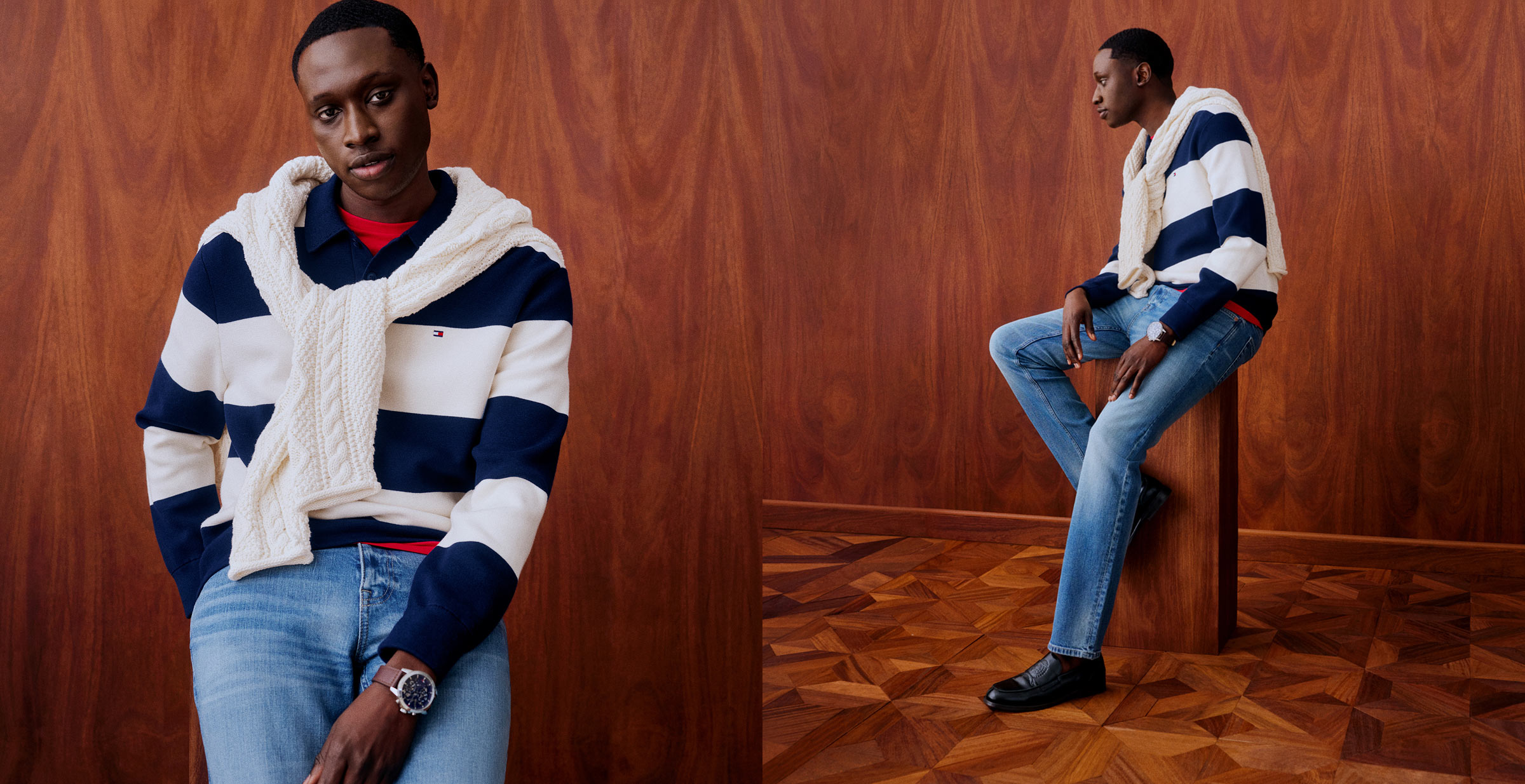 Man wearing a navy and white striped Tommy Hilfiger cable knit sweater over a red shirt with blue jeans, posing against a wooden backdrop