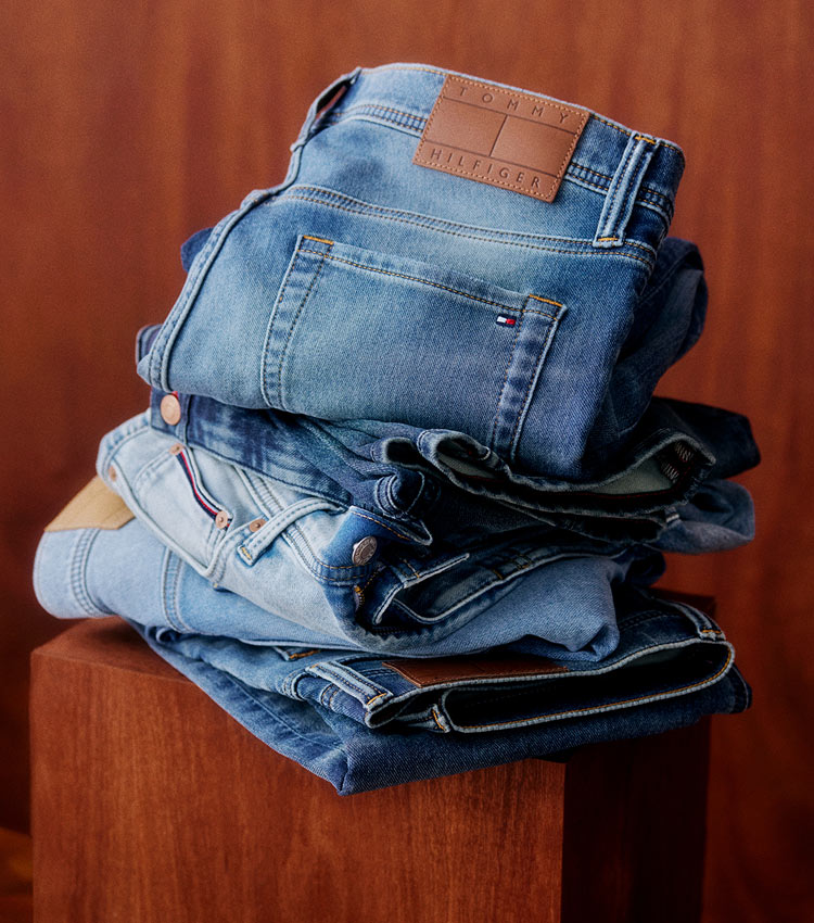 Stack of folded Tommy Hilfiger jeans in assorted blue washes, placed on a wooden surface.