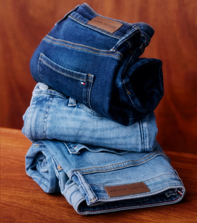 Stack of folded Tommy Hilfiger jeans in assorted blue washes, placed on a wooden surface.