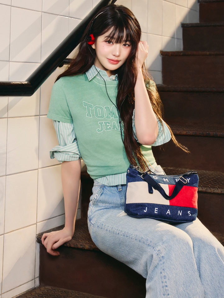 Won Young posing on tiled subway steps wearing a mint green Tommy Hilfiger top, jeans, and a red, white, and blue crossbody bag.
