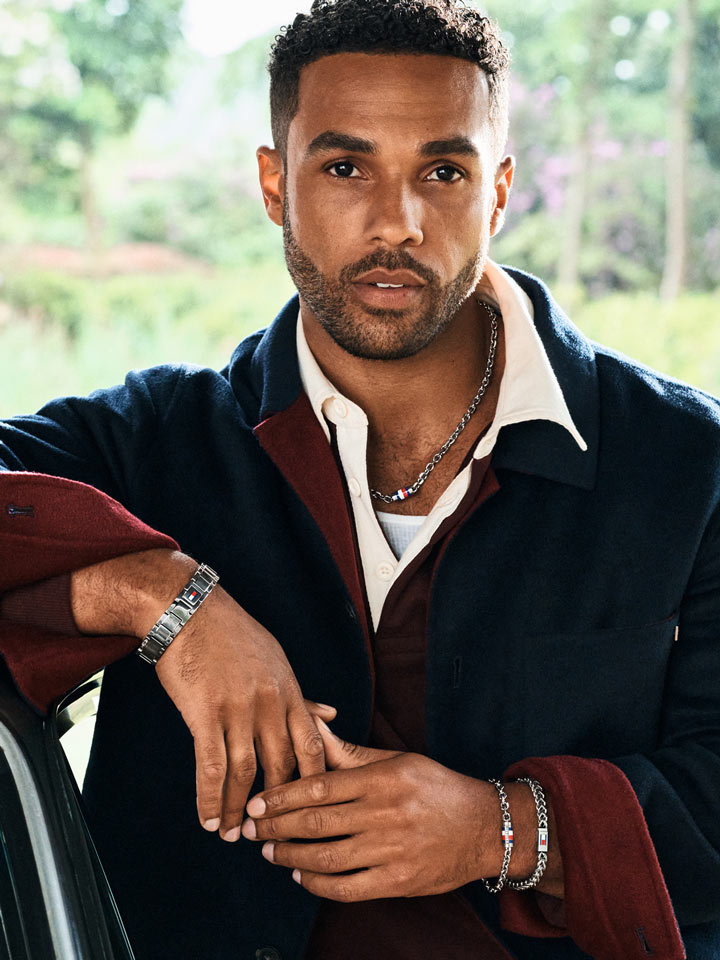 Model wearing a colorblock jacket, layered with silver-toned Tommy Hilfiger bracelets and chains, posing with a confident expression.