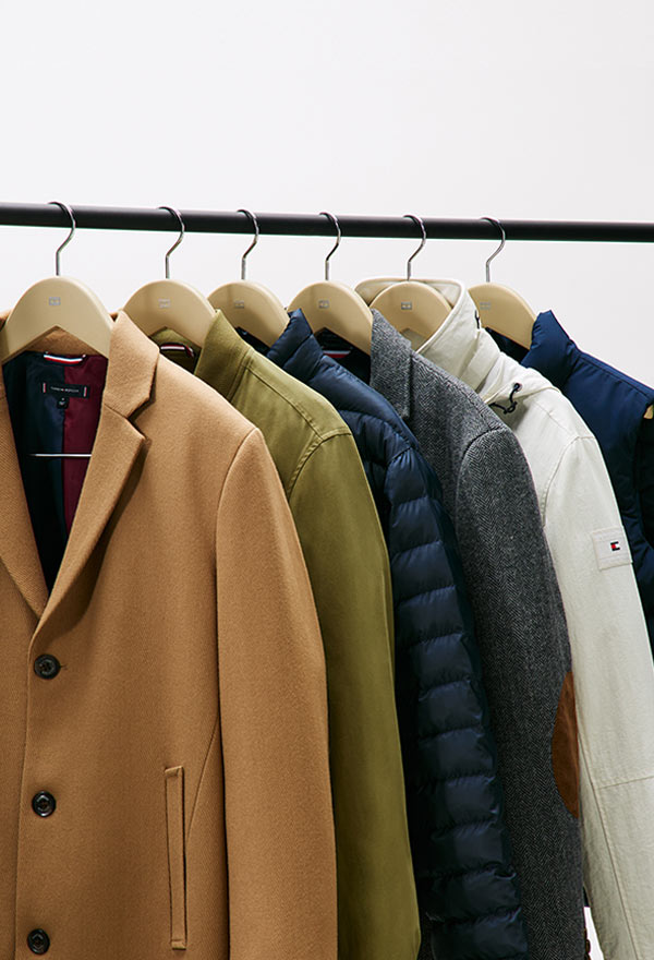 Clothing rack featuring Tommy Hilfiger men's outerwear, including wool coats, puffers, quilted jackets, and down parkas in neutral and navy tones.