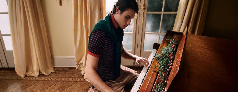 Model indoor sitting playing the piano wearing a navy Tommy Hilfiger Polo