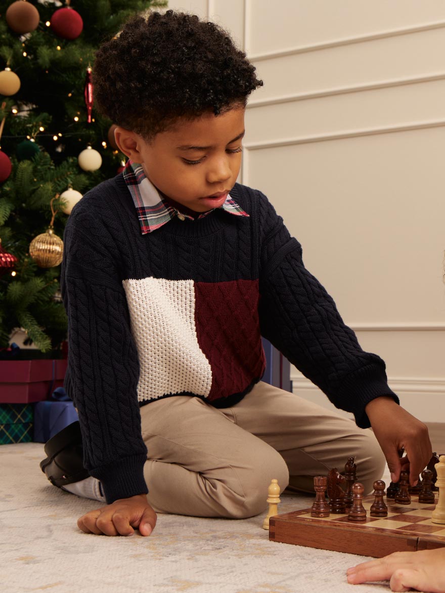 Young model sitting on the ground playing with toys wearing a Tommy Hilfiger Sweater