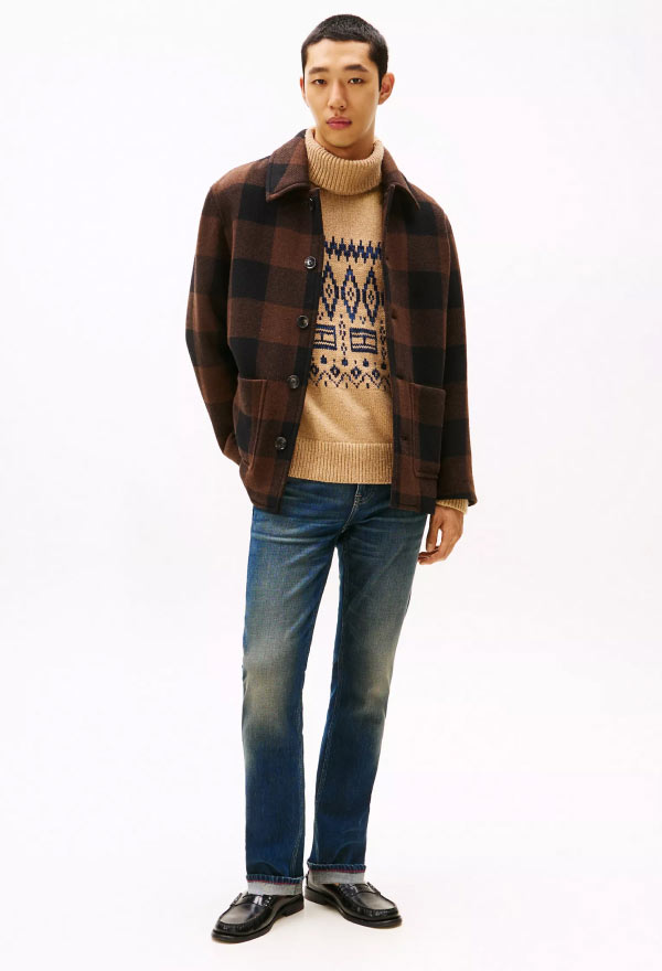 Model dressed in a Tommy Hilfiger plaid overshirt layered over a striped shirt and paired with dark denim jeans.
