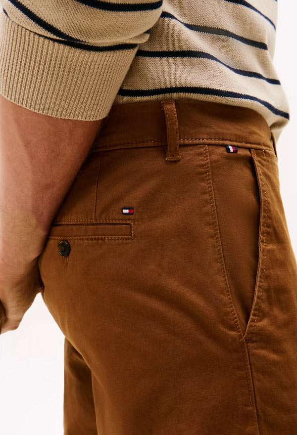 Close-up of a model wearing brown Tommy Hilfiger pants, featuring the signature flag embroidery on the back pocket.