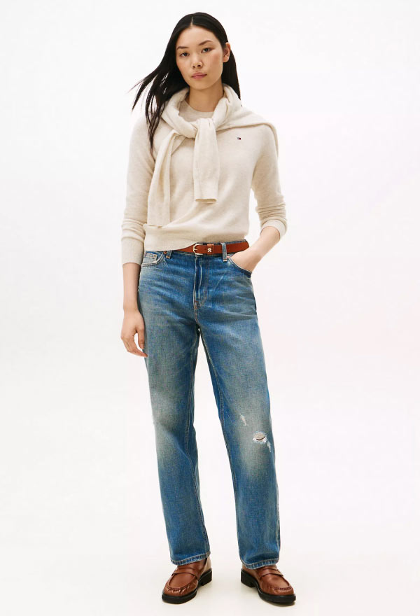 Model wearing a cream button-down Tommy Hilfiger shirt tucked into relaxed-fit distressed jeans, paired with loafers.