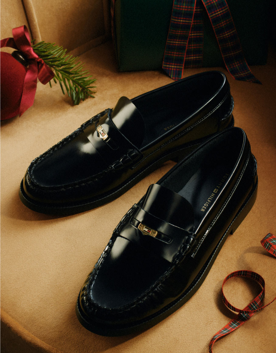 Polished navy Tommy Hilfiger tassel loafers on a gift-wrapping table with ribbon and scissors.