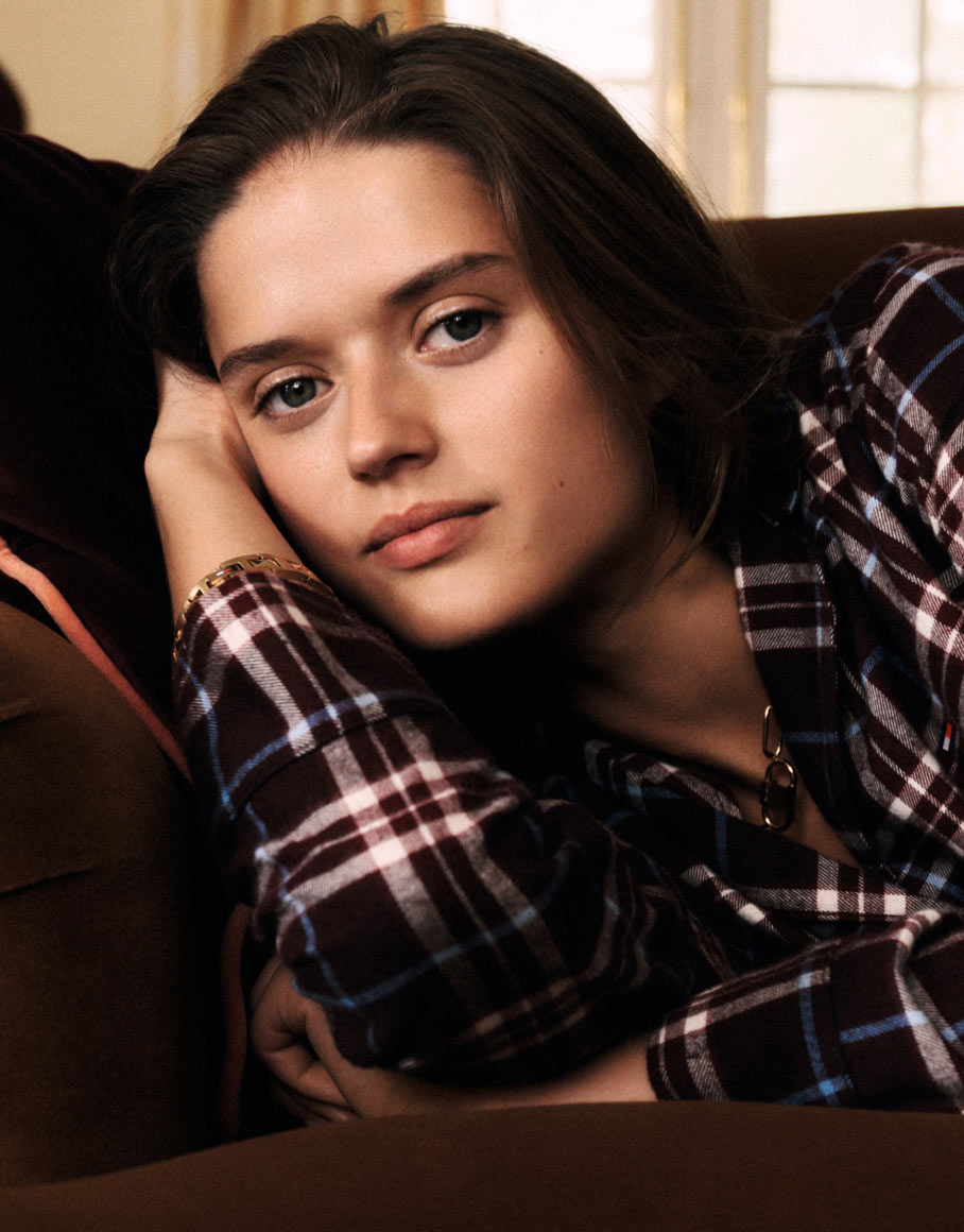 Model reclining on a sofa in a dark plaid Tommy Hilfiger flannel button-down, indoor cozy setting.