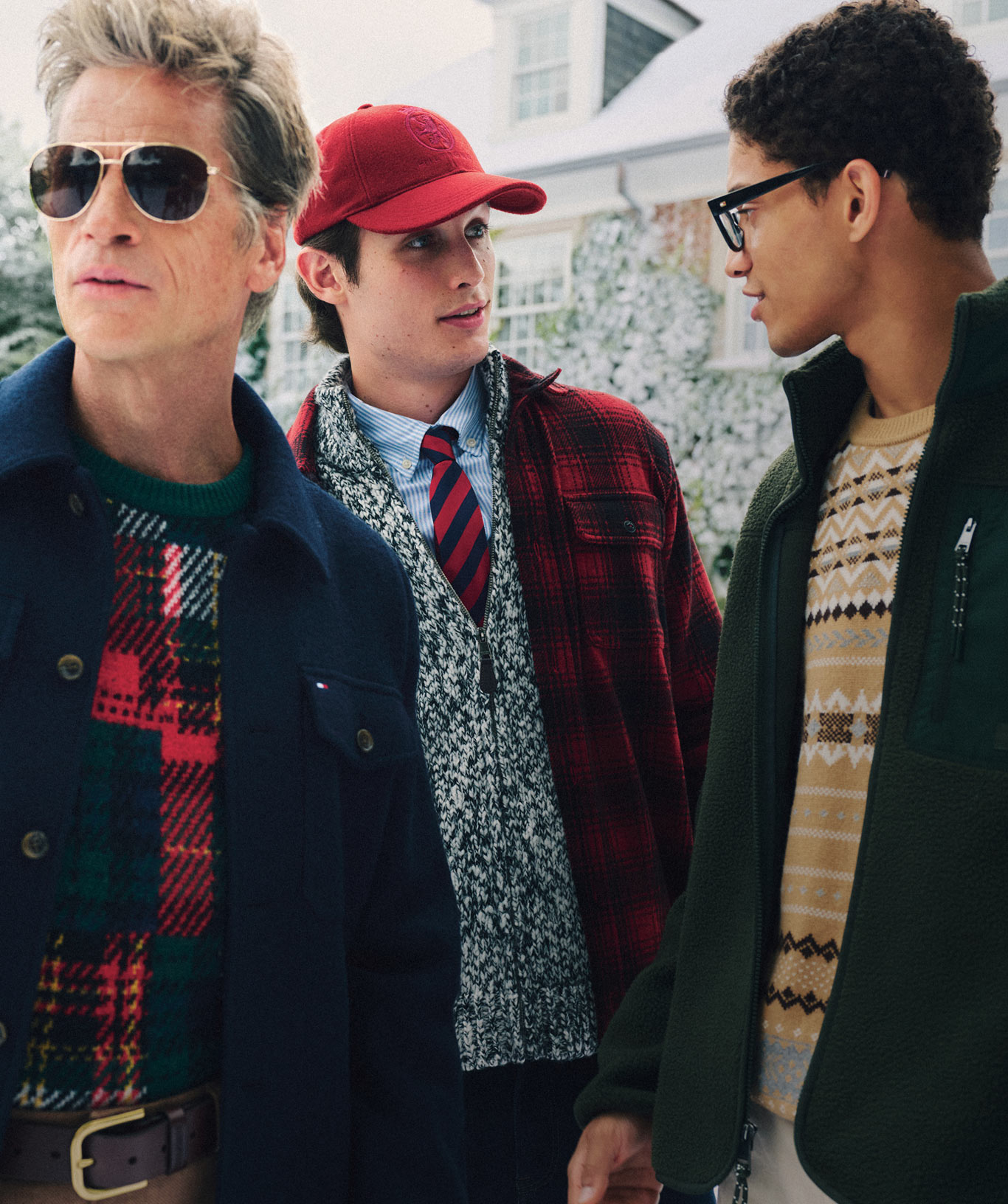 Group of models outdoors in Tommy Hilfiger novelty sweaters—plaid, argyle, and intarsia—chatting on a winter street.