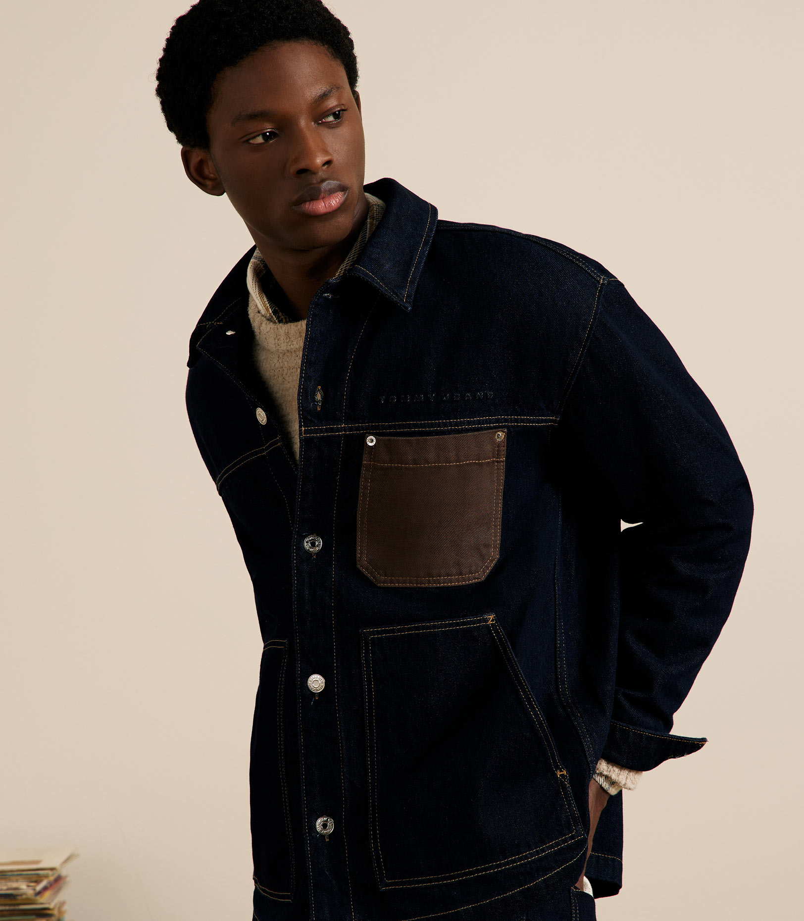 Model in a dark denim Tommy Jeans chore jacket with contrast brown pocket and collar, shot in a neutral studio.