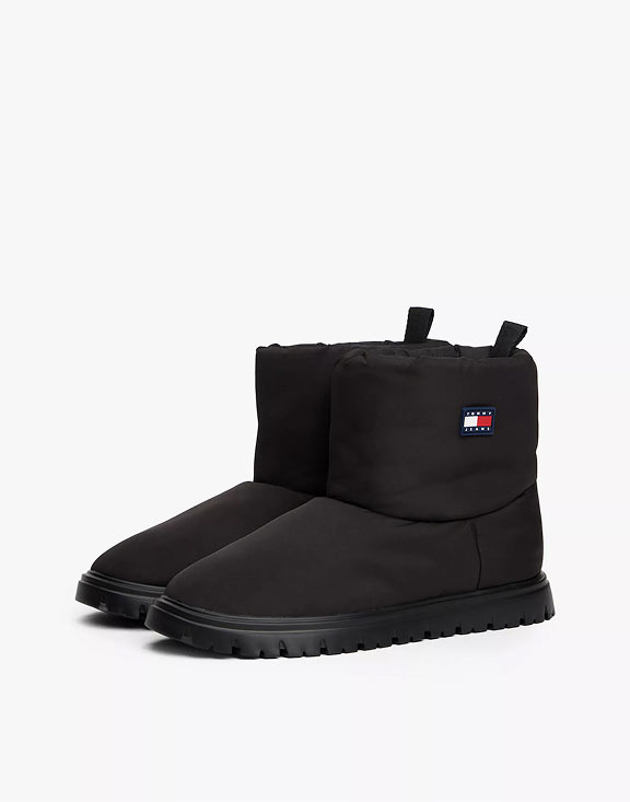 Black Tommy Jeans ankle boots with a lug sole and side flag patch, shown on a studio tabletop.