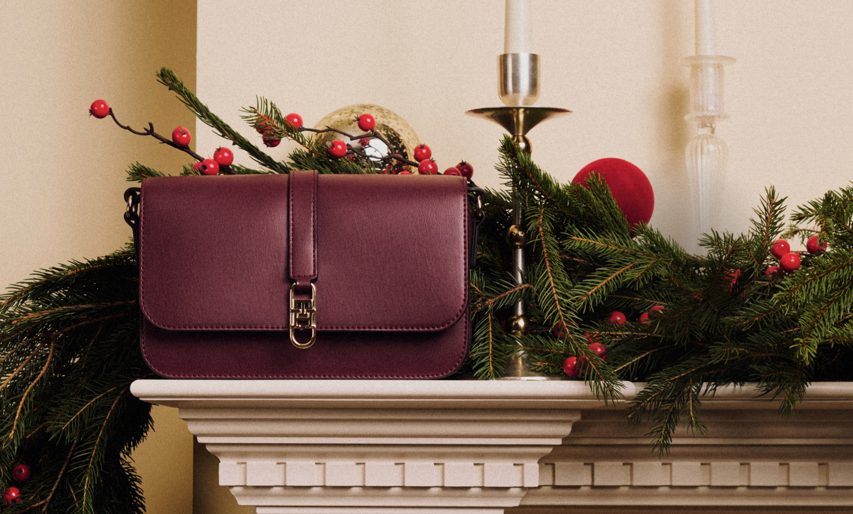 Burgundy Tommy Hilfiger shoulder bag styled on a garlanded mantel with taper candles
