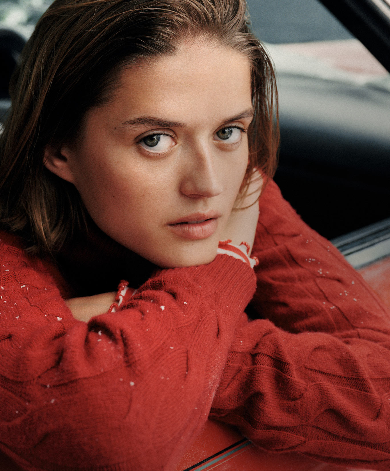 A close-up of a model in a red Tommy Hilfiger knit, shot outdoors by a car in the snow.