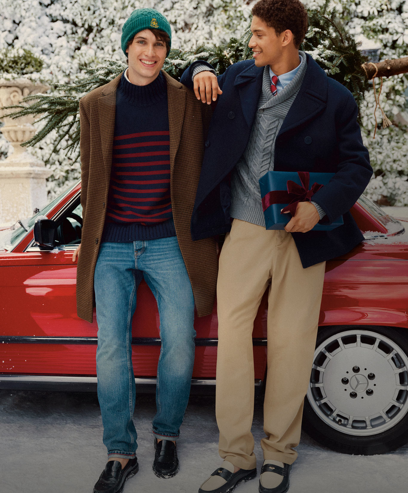 Two models in Tommy Hilfiger winter layers by a red car in the snow