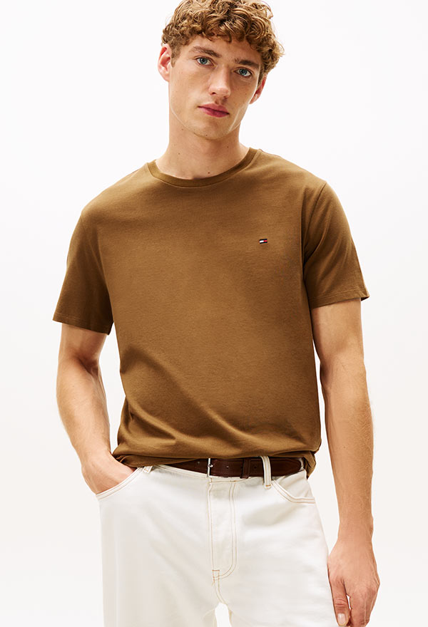 Model wearing a Tommy Hilfiger olive green short-sleeve polo shirt with contrast tipping, styled with white pants, against a white background