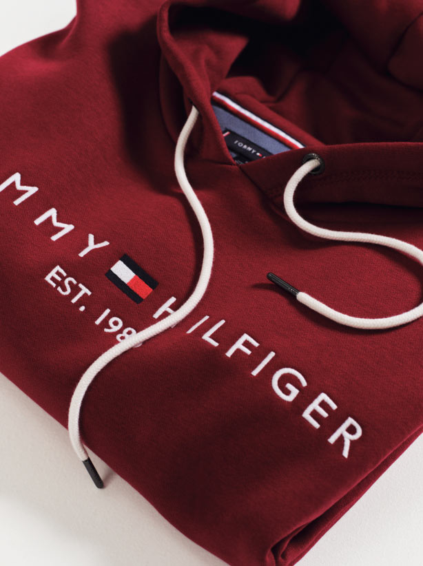 A folded red Tommy Hilfiger hoodie with a drawstring and the Tommy Hilfiger logo and flag across the front.