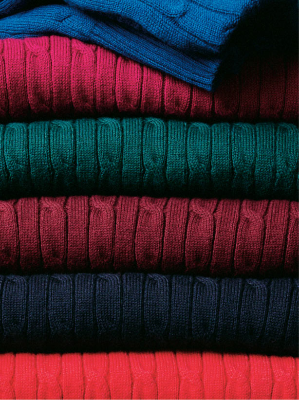 Stack of folded Tommy Hilfiger ribbed knit sweaters in multiple colors, including teal, green, navy, and red.