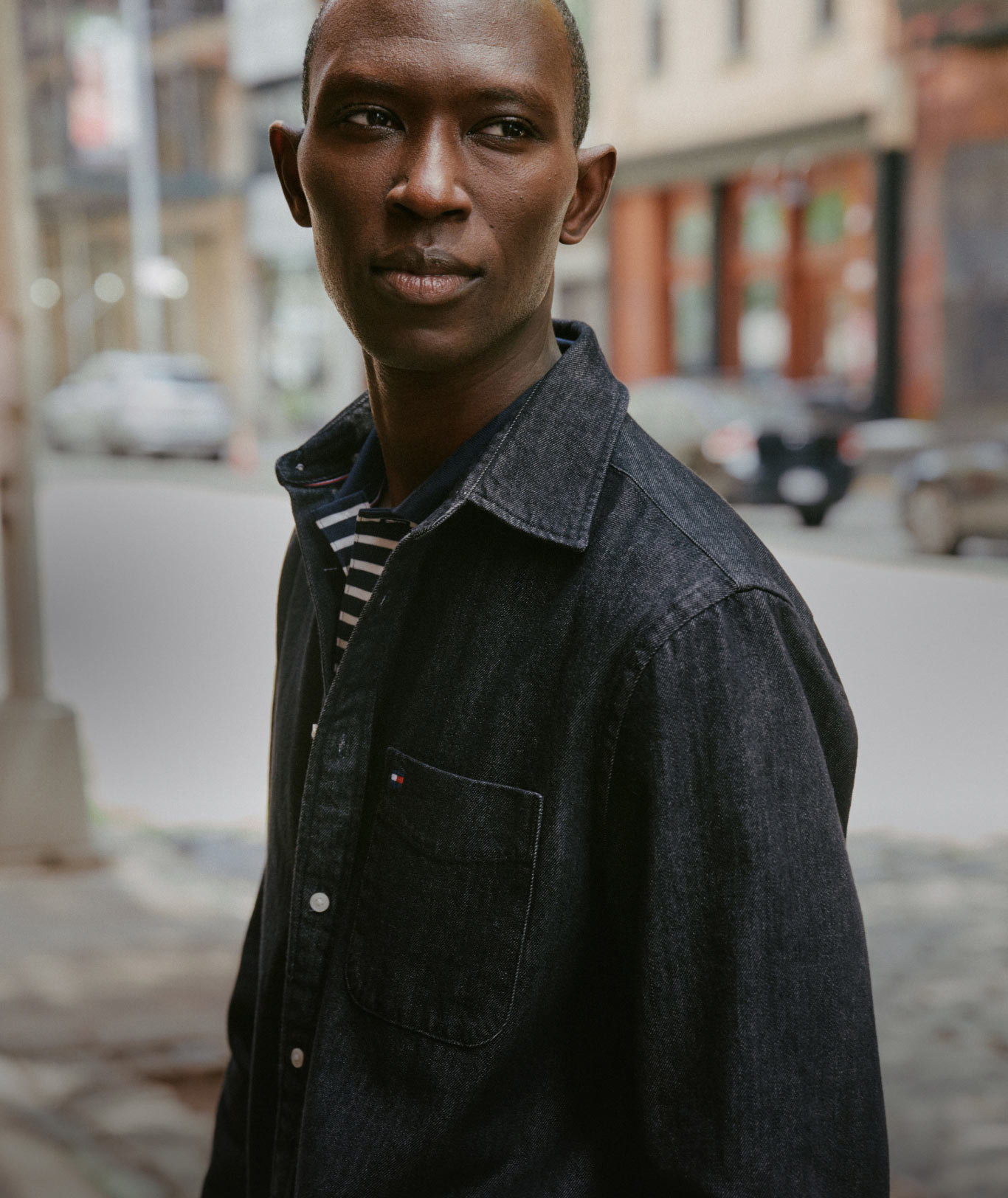 A model in Tommy Hilfiger denim and outerwear on a city street, with one model in a dark jacket and wide leg jeans and another model in a black jacket in the foreground.