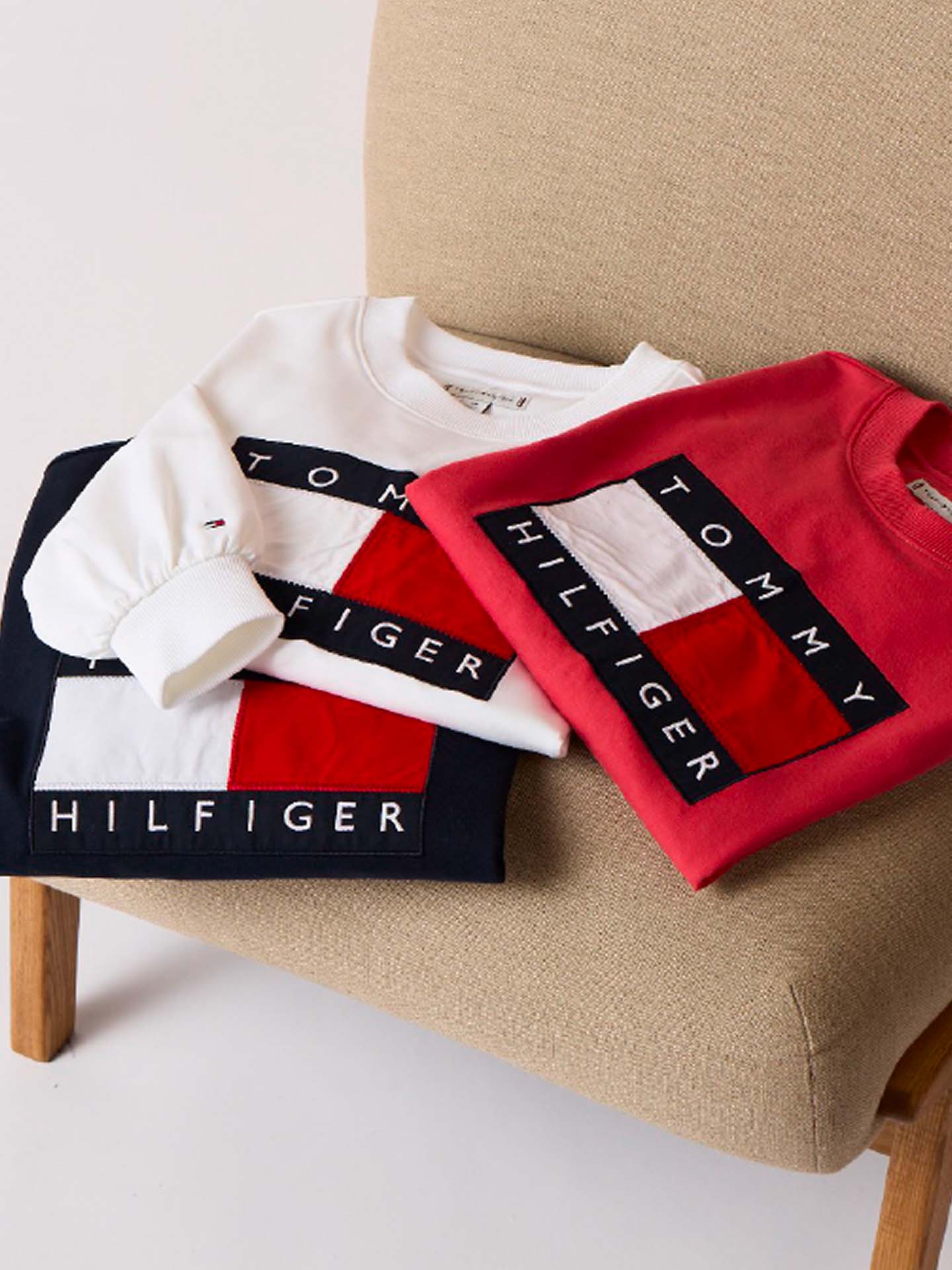 A set of Tommy Hilfiger big flag logo t-shirts piled on top of a chair.