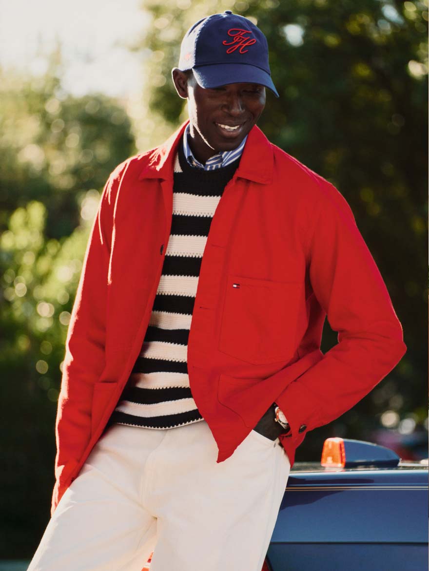 Male model wearing a Tommy Hilfiger red jacket, off white pants and a colorblock sweater