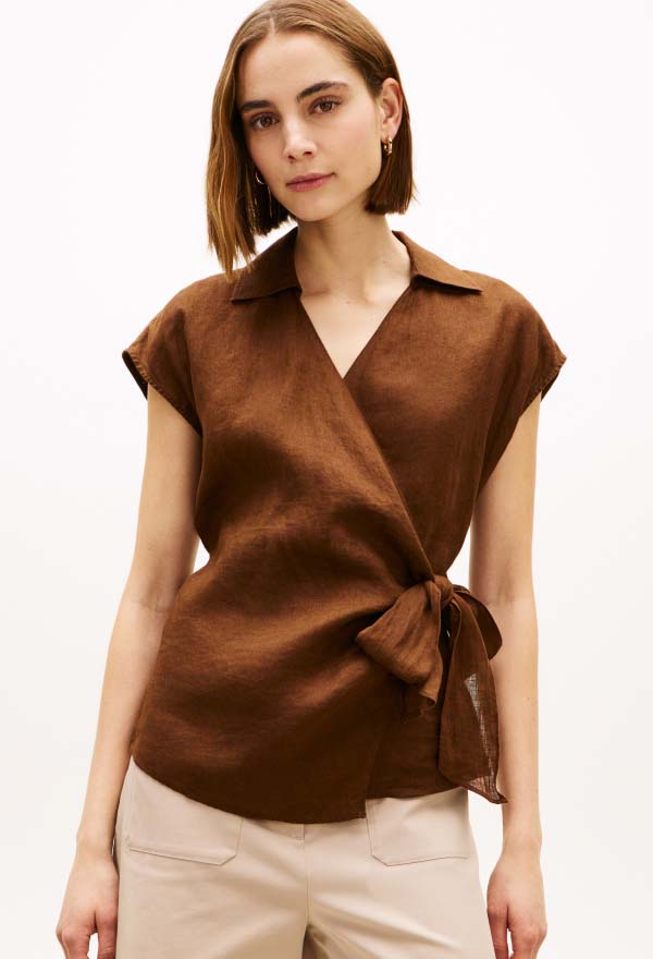 Model wearing a brown Tommy Hilfiger sleeveless wrap-style top with a tie waist, posed against a plain studio background.