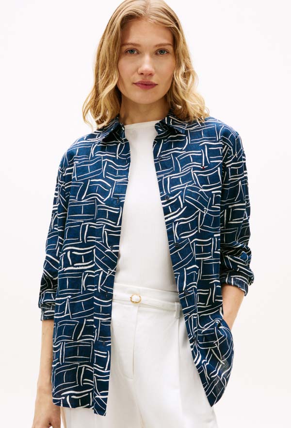 Model wearing a blue patterned Tommy Hilfiger zip-front jacket over a white top, styled with white bottoms in a clean studio setting.