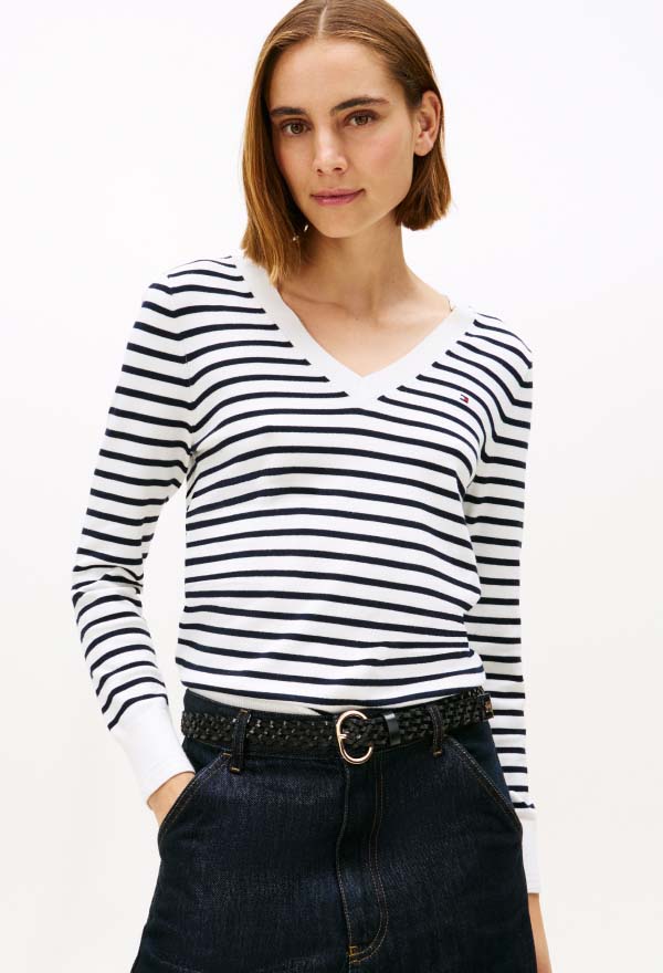 Model wearing a black-and-white striped Tommy Hilfiger long-sleeve top, styled with dark jeans and a black belt in a studio setting.
